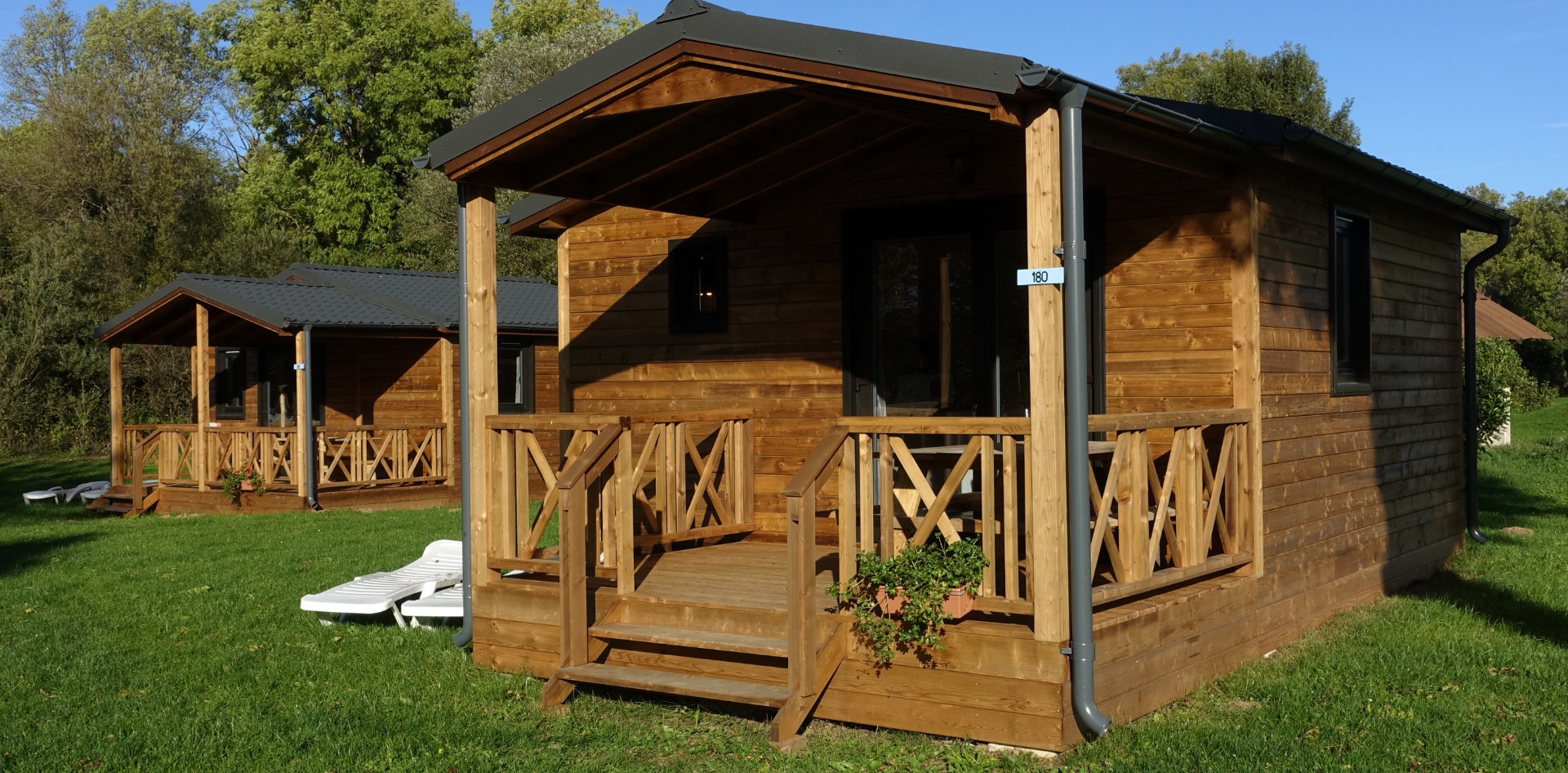 View of the Monia Chalet with covered wood terrace to rent at Les Bords de Loue campsite in Jura