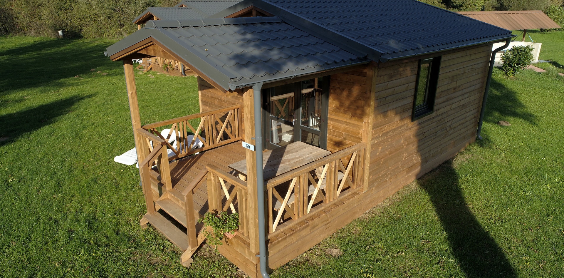 Vue aérienne du chalet Monia avec terrasse en bois couverte en location au camping les Bords de Loue, dans le Jura à Parcey