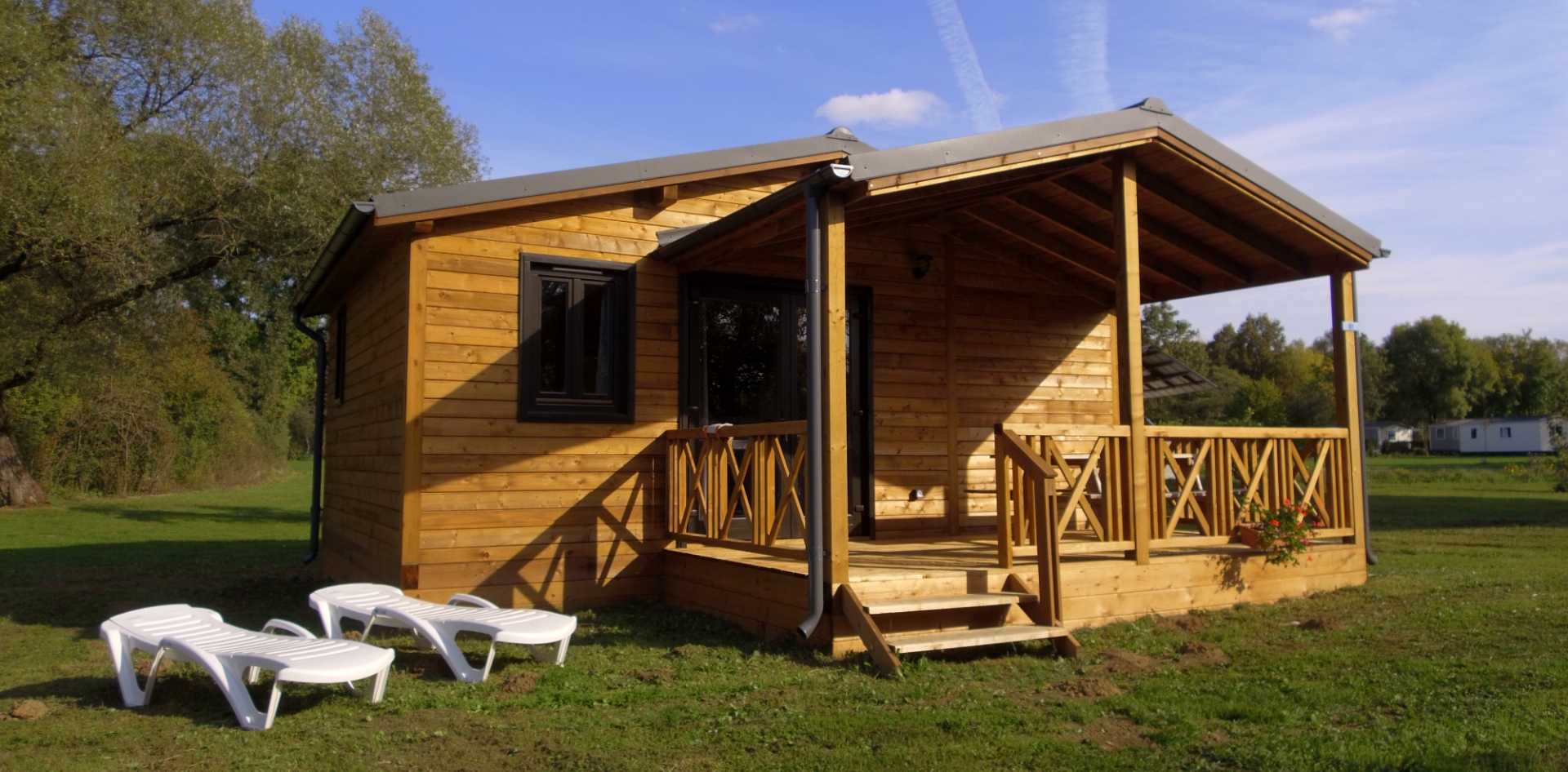 Ansicht des Chalets Savania mit überdachter Holzterrasse, zu vermieten auf dem Campingplatz Les Bords de Loue im Jura