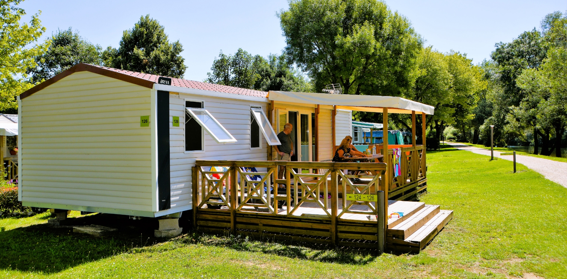 Vue du mobil-home Quattro avec terrasse en bois couverte en location au camping les Bords de Loue dans le Jura