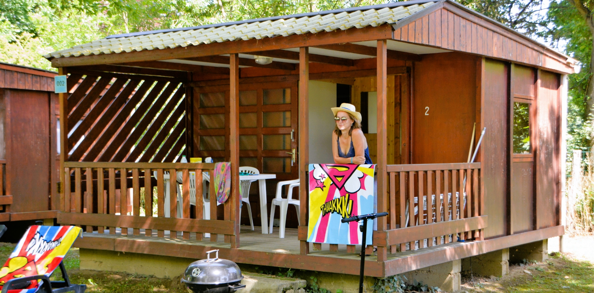 Außenansicht des kleinen Chalets mit überdachter Holzterrasse, zu vermieten auf dem Campingplatz Les Bords de Loue im Jura